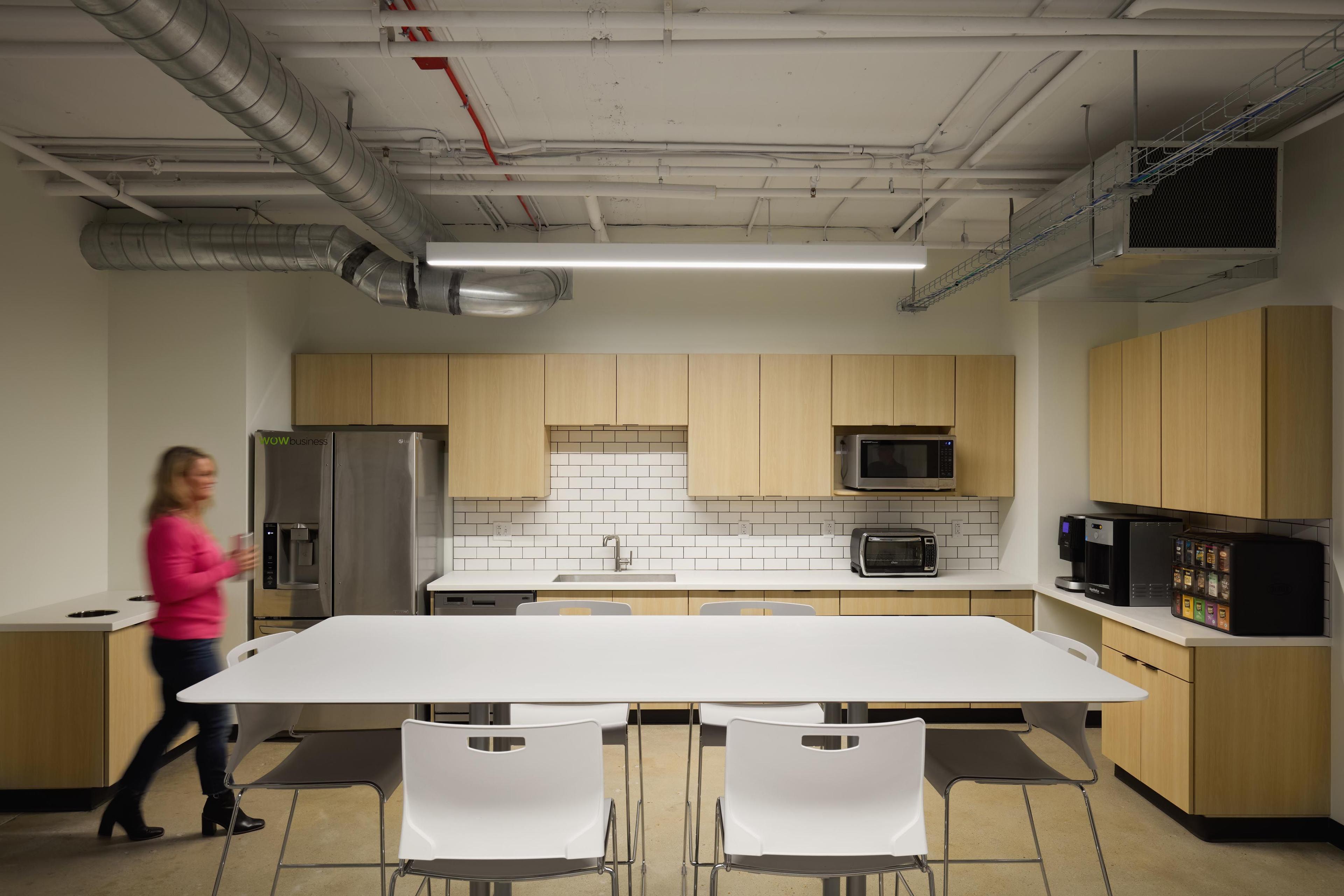 Woman walking through a breakroom with tables, chairs, and cabinets