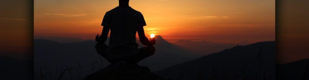 Person meditating on a mountain during sunset